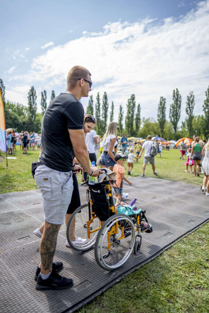 na utwardzonym terenie znajduje się ojciec z dzieckiem z niepełnosprawnością na wózku 